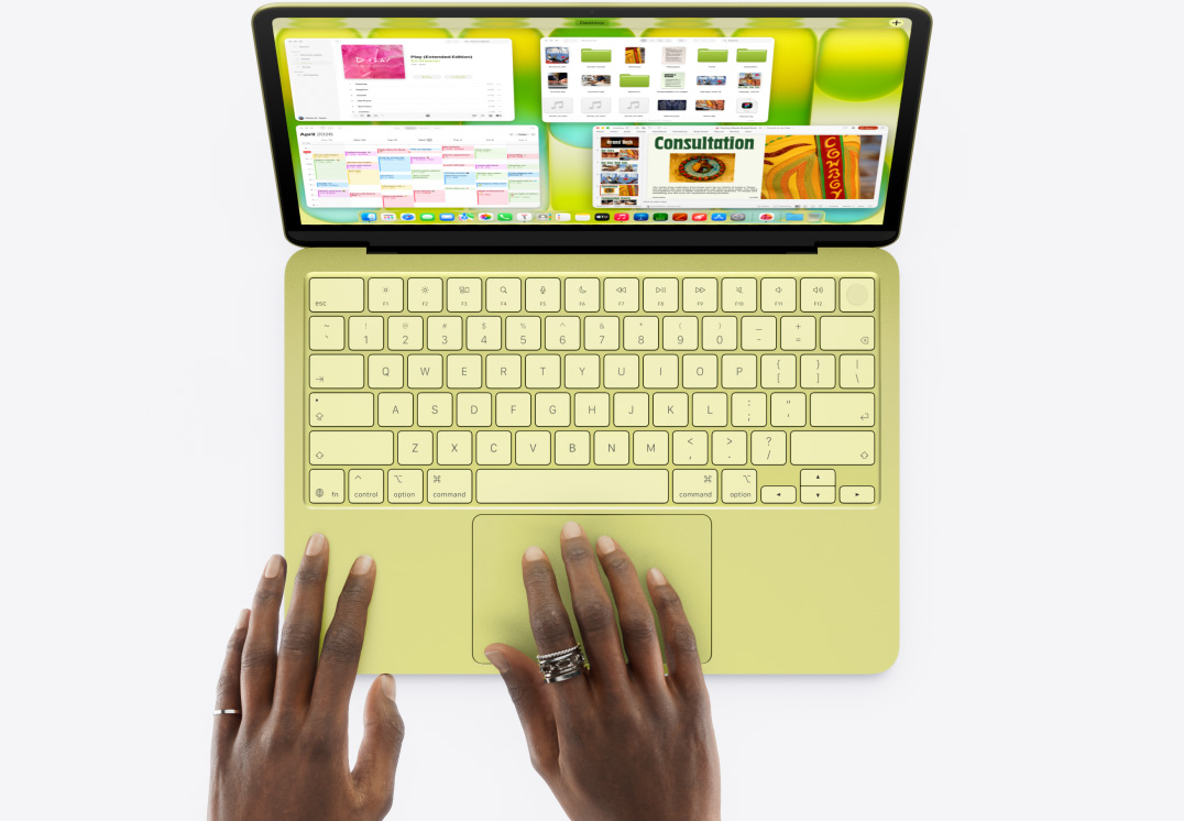MacBook Neo, σε χρώμα κίτρο, χέρι ατόμου στο trackpad, πολλά παράθυρα ανοιχτά, συμπεριλαμβανομένων των εφαρμογών Μουσική, Ημερολόγιο και Microsoft PowerPoint