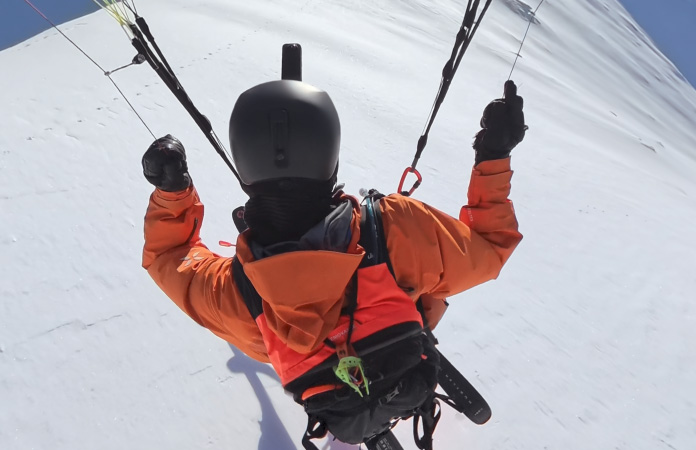 Person, die mit einem Paraski durch die Luft über einen geschwungenen Berggipfel fliegt, mit weitem Sichtfeld